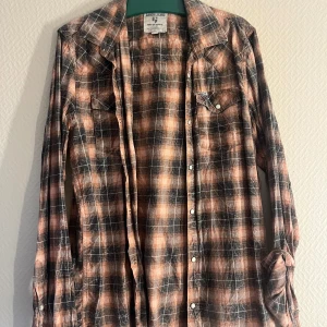 Rutig skjorta från Garcia Jeans - Snygg rutig skjorta från Garcia Jeans i svart och orange. Skjortan har långa ärmar och knappar framtill. Perfekt för en avslappnad stil med en touch av färg.