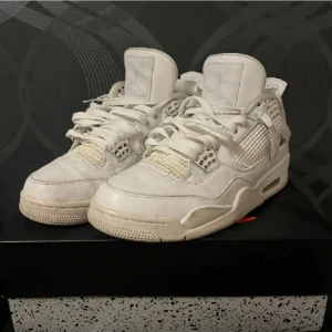  Jordan 4  - Säljer ett par klassiska vita Jordans med snörning och ikonisk Jumpman-logga på hälen. Skorna har en robust design med vadderad krage och perforerade detaljer för ventilation.