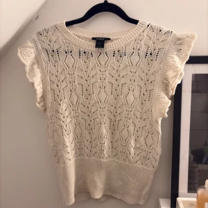 Vit stickad topp från Lindex - Säljer en söt vit stickad topp från Lindex med vackert spetsmönster och volangdetaljer vid ärmarna. Perfekt för sommaren💞