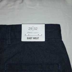 Mörkblå byxor från East West/ från Brothers  - Snygga mörkblå byxor från East West i stretchigt material. De har en slim fit passform och är perfekta för en stilren look. Byxorna har en klassisk design med dragkedja och knapp framtill. Priset kan diskuteras 