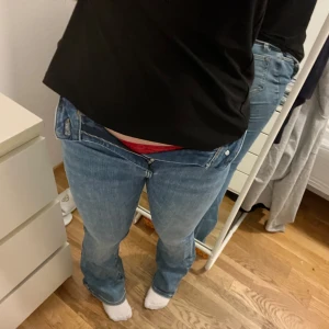 Blå jeans med bootcut - Säljer ett par klassiska blå jeans med bootcut. De har en lågmidjad passform och är perfekta för en avslappnad stil. Jeansen har en dragkedja och knappar framtill.