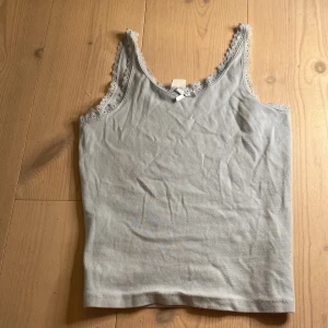 Ljusblå linnetopp från Lindex - Säljer en söt ljusblå linnetopp från Lindex med spetsdetaljer runt halsringningen och axelbanden. Toppen har en liten rosett framtill och är perfekt för varma dagar. Tillverkad i mjukt material för extra komfort. Ser bättre ut på💛 ny 