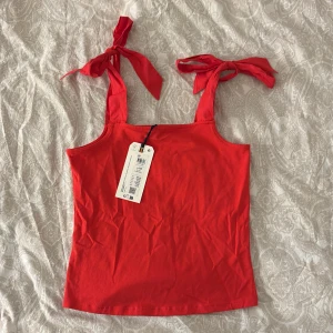 Röd linnetopp med knytband - Snygg röd topp från Lindex med knytband på axlarna. Perfekt för sommardagar och ger en fräsch look. Toppen är i ett mjukt material som sitter bekvämt på kroppen. Toppen skulle passa perfekt på en kräftskiva i höstdagarna! Toppen är aldrig använd, enbart testad på bilden. Nypris 199, säljer för 100!