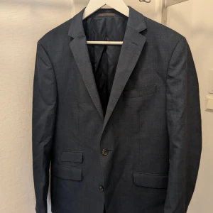Mörkblå kavaj från Riley - Snygg mörkblå kavaj från Riley i slim fit. Kavajen har två knappar framtill och klassiska fickor. Perfekt för en stilren look.