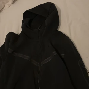 Svart hoodie från Nike - Säljer en svart hoodie från Nike med dragkedja och huva. Perfekt för en casual look. Den har långa ärmar och är tillverkad i ett mjukt material.