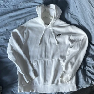 Vit hoodie från Nike - Säljer en klassisk vit hoodie från Nike med en liten svart logga på bröstet. Den har en stor ficka framtill och justerbar luva