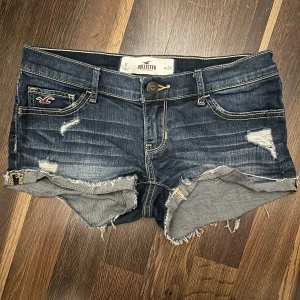 Mörkblå jeansshorts från Hollister - Intressekoll på mina snygga mörkblå jeansshorts från Hollister med slitna detaljer och fransiga kanter. Perfekta för en avslappnad stil. De har en knapp och dragkedja framtill samt klassiska fem fickor. Skicka gärna prisförslag 🤍
