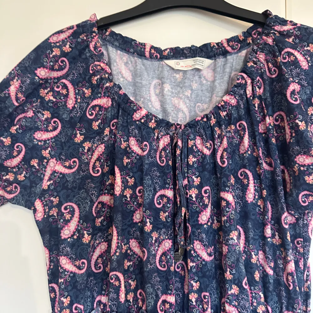Charmig klänning från Indiska med ett färgglatt paisleymönster i rosa och blått. Klänningen har korta ärmar och en volangdetalj vid fållen. Perfekt för en somrig look! Från märket Odd Molly i storlek 1 som enligt deras storleksguide motsvarar en storlek S. Kan vara något rymlig i storlek. Mycket fint skick, jag hittar inga synliga anmärkningar eller defekter. . Mekot.