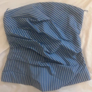 Blå och vit randig tubtopp - Snygg blå tubtopp med vita ränder. Perfekt för sommardagar eller en avslappnad stil. Toppen är axelbandslös och har en stilren design som passar till många olika outfits.