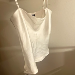 Vit satinlinne från Gina Tricot - Snyggt vitt satinlinne från Gina Tricot med smala axelband och en elegant drapering framtill. Perfekt för en stilren look.