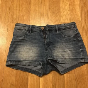 Blå jeansshorts från A Denim - Snygga blå jeansshorts från A Denim med klassisk femficksdesign och dragkedja. Perfekta för en avslappnad stil. De har en lätt tvättad look som ger en cool vibe.