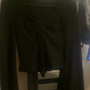 Svart ribbad topp med knyt - Snygg svart ribbad topp med långa ärmar och knytning framtill. Perfekt för en stilren look.