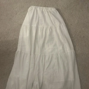 Vit långkjol - Säljer en stilren vit långkjol med en luftig och bekväm passform. Kjolen har en tight midja. Den är tillverkad i ett lätt material som ger en skön känsla, med dubbelt linne lager, perfekt inför sommaren!