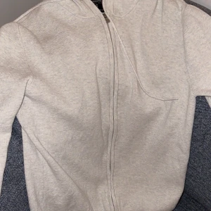 Grå/vit tröja med zip - Oanvänd vit/grå tröja med zip. Säljes av just den anledningen, att den inte har blivit använd. 