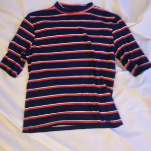 Randig tröja från H&M - Säljer en randig tröja från H&M i marinblått med röda och vita ränder. Tröjan har trekvartsärmar och en högre krage. Perfekt för en avslappnad stil. Hör av dig vid intresse!