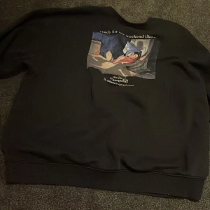Svart Disney Fantasia tröja - Säljer en svart tröja från H&M med ett tryck av Disney's Fantasia. Tröjan har en bild av Musse Pigg och texten 'ready for the weekend like...'. Perfekt för alla Disney-fans!