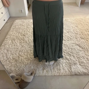 Grön långkjol - Snygg grön långkjol i ett mjukt och flödande material. Kjolen har en avslappnad passform och en diskret volangdetalj nedtill som ger en fin rörelse. Perfekt för en bohemisk look eller en avslappnad dag ute. Passar bra med en enkel topp eller stickad tröja.
