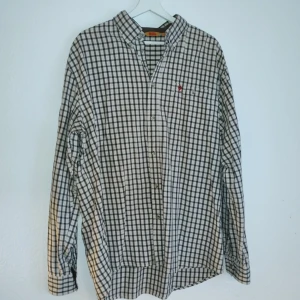 Rutig skjorta från Fjällräven - Säljer en snygg rutig skjorta från Fjällräven i storlek XXL. Skjortan har ett klassiskt rutmönster i svart och vitt med en liten broderad logga på bröstet. Perfekt för en avslappnad stil med långa ärmar och knappar framtill.