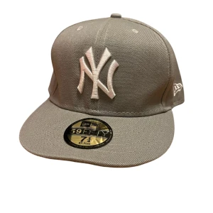 Grå keps från New Era - Snygg grå keps från New Era med broderad logotyp framtill. Perfekt för en stilren look. Kepsen har en klassisk design med en rak skärm och är tillverkad i bomull. Osäker på äkt skap då jag köpte den på Vinted🙂 strl 57,7 men sitter lite större