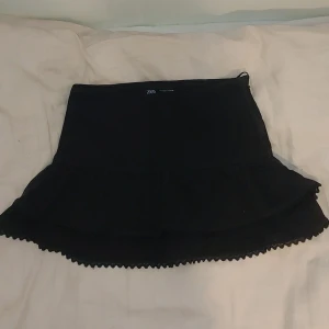 Svart kortkjol från Zara - Snygg svart kortkjol från Zara med volangdetaljer. Perfekt för att skapa en stilren look. Kjolen har en enkel design som gör den lätt att matcha med olika toppar.