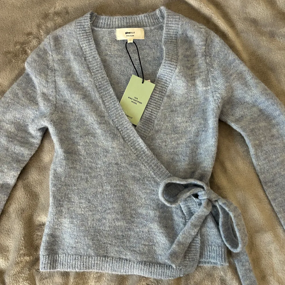 Säljer en mysig gråblå omlottkofta från Gina Tricot i ullblandning. Koftan har långa ärmar och knytband i midjan för en justerbar passform. Perfekt för kyliga dagar! 🧶. Neuletakit & Villapaidat.