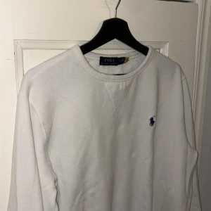 Vit tröja från Ralph Lauren - Säljer en klassisk vit tröja från Ralph Lauren med rund hals och det ikoniska blå logotypbroderiet på bröstet. Perfekt för en stilren och avslappnad look.
