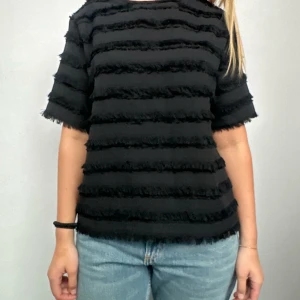 Svart randig topp - Säljer en svart topp med horisontella ränder och korta ärmar. Toppen har en unik textur med fransiga detaljer som ger en cool look. Perfekt för att ge din outfit en extra edge.