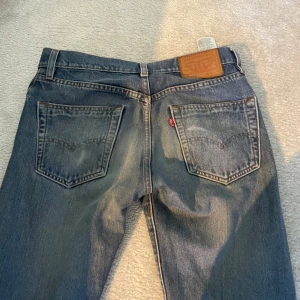 Levis 501 jeans - Klassiska Levis 501 jeans i blå denim med knappgylf. De har en rak passform och är i storlek W28 L32. Perfekta för en tidlös stil.