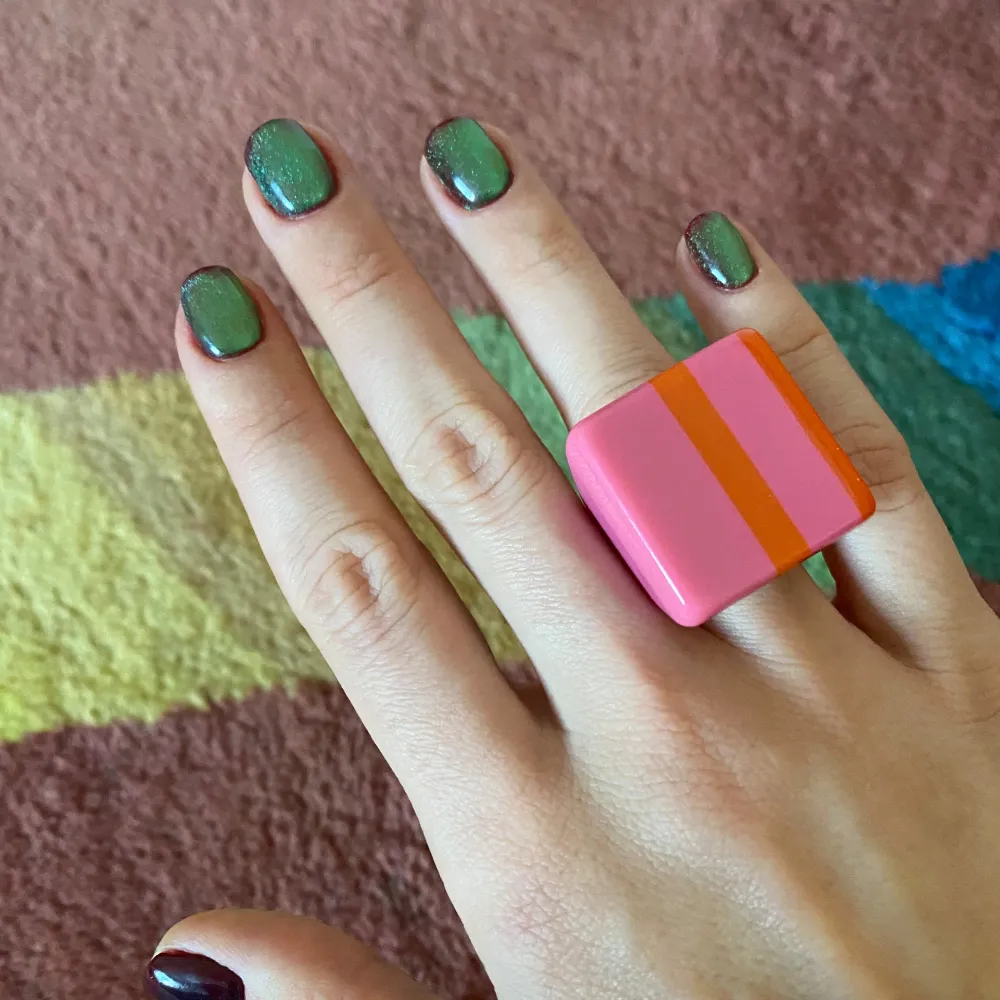 Säljer en färgglad hartsring med randigt mönster i rosa och orange. Ringen har en iögonfallande design som verkligen sticker ut. Storlek: 18,5 mm. Asusteet.