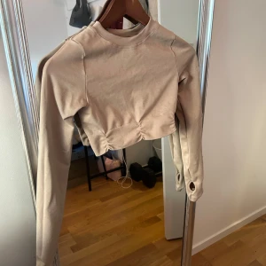 Beige croppad tröja från Chiquelle - Säljer en beige croppad tröja från Chiquelle Activewear. Tröjan har långa ärmar och en stilren design, perfekt för en avslappnad look. Materialet känns mjukt och bekvämt, idealiskt för vardagsbruk och träning