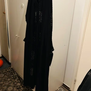 Svart långklänning/ Abaya med broderade detaljer - Elegant svart långklänning/ Abaya med vackra broderade detaljer i guld. Klänningen har en lös passform och långa ärmar, perfekt för en stilfull look. Den är tillverkad i ett mjukt och bekvämt material.