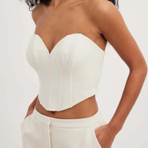 Vit korsett-topp - Snygg vit korsett-topp från nakd, med hjärtformad urringning och smockad rygg. Toppen är axelbandslös och har en figurnära passform som framhäver midjan. Använd endast 2 gånger!