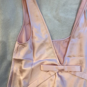Rosa satinlinne från ASOS - Rosa satinlinne från ASOS med djup v-ringning och rosett på ryggen samt u-ringning framtill. Mycket bra skick, oanvänd.💕