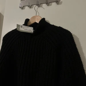 Svart stickad tröja - Säljer en stilren svart stickad tröja med hög krage. Tröjan har långa ärmar och en ribbad design som ger en mysig känsla. Perfekt för kyligare dagar. Prislapp kvar 