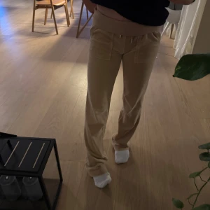 Beige mjukisbyxor från Juicy Couture - Säljer ett par bekväma och stiliga beige mjukisbyxor från Juicy Couture. Byxorna har en tight passform och är tillverkade i mjukt material med snörning i midjan. Perfekta för en avslappnad look.