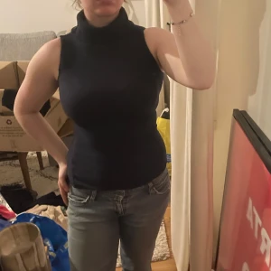 Svart ärmlös polotopp - Snygg svart ärmlös polotopp i ett stretchigt material. Perfekt för lager-på-lager eller att bära som den är. Enkel och stilren design som passar till många olika outfits.