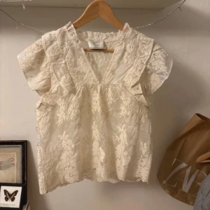 Vit spetsblus från Neo Noir - Säljer en vacker vit spetsblus från Neo Noir. Blusen har en v-ringad design med korta ärmar och fina spetsdetaljer. Perfekt för en elegant look. Aldrig andvänd💗💗