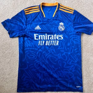 Blå Real Madrid fotbollströja från Adidas - Säljer en blå Real Madrid fotbollströja från Adidas. Fick den i julklapp men den passar inte så därför sälj den. 