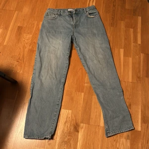 Blå jeansbyxor - Säljer ett par klassiska blå jeansbyxor med rak passform. De har en midwaist design och är tillverkade i slitstarkt denim. Byxorna har en dragkedja och knapp framtill samt fem fickor. Perfekta för en avslappnad stil.