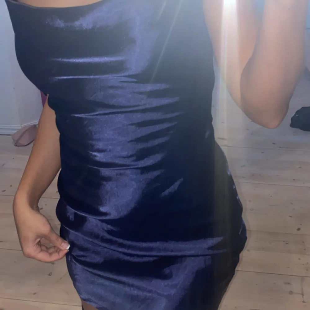 Snygg mörkblå kortklänning i satin med smala axelband. Perfekt för en kväll ute eller en speciell tillställning. Klänningen har en elegant och glansig finish som ger en lyxig känsla.. Mekot.