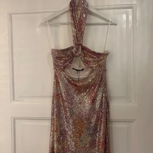 Glittrig långklänning med halterneck - Säljer en fantastisk glittrig långklänning med halterneck-design. Klänningen har en skimrande yta i rosa och guldtoner, perfekt för en festlig kväll. Den har en elegant passform och en unik knytning vid halsen. Perfekt för att glänsa på nästa event! ✨