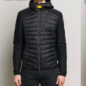 Svart hybridjacka med huva - Snygg svart hybridjacka från Parajumpers med quiltad front och huva. Jackan har en dragkedja och en bröstficka med dragkedja. Perfekt för en stilren look. Och det är bara skriva om ni är intresserade och självklart så får ni bilder om ni frågar 
