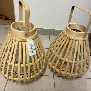 Två stora bambulyktor - Säljer två stora bambulyktor med glasinsats. Perfekta för att skapa en mysig stämning både inomhus och utomhus. De har en naturlig träfärg och ett praktiskt handtag för enkel förflyttning. Passar utmärkt för blockljus eller LED-ljus.