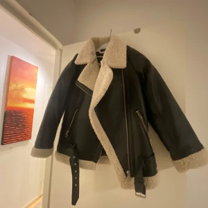 Svart skinnjacka med pälsfoder - Snygg svart skinnjacka med mjukt pälsfoder och detaljer som dragkedja och bälte. Perfekt för kyliga dagar med sin stilrena design och bekväma passform. Denna köpte jag från hm för 700 och använt den 1 gång. Säljer pga för stor storlek.