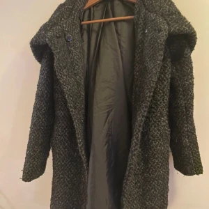 Grå kappa med stor krage - Snygg grå kappa med en stor och mysig krage. Perfekt för kyliga dagar. Kappan har en stilren design med knappar framtill och är tillverkad i ett tjockt material som håller dig varm.