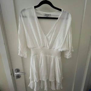 Vit klänning från Amisu - Säljer en vit klänning från Amisu med v-ringning och trekvartsärmar. Klänningen har en omlott-design och volangdetaljer vid fållen. Perfekt för sommarens alla tillfällen. 🌸