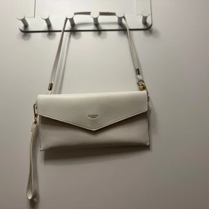 Vit axelväska  - Snygg vit axelväska. Väskan har en praktisk dragkedja och en avtagbar axelrem, vilket gör den mångsidig och lätt att bära. Perfekt för att hålla dina nödvändigheter organiserade och inom räckhåll 💓