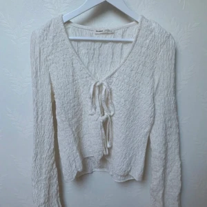 Vit ribbad tröja med knyt - Säljer en vit ribbad tröja från Bershkamed v-ringning och knyt framtill i stolen S. Tröjan har långa ärmar och en mjuk, vågig textur. Endast använd en gång annars är den som ny 💕