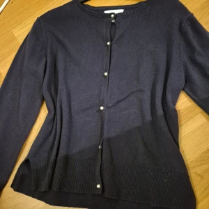 Mörkblå kofta från Zara - Säljer en stilren mörkblå kofta från Zara med knappar framtill. Koftan har långa ärmar och ribbade kanter vid ärmslut och nederkant. Perfekt för kyligare dagar. Dekorerad med pärlemorknappar