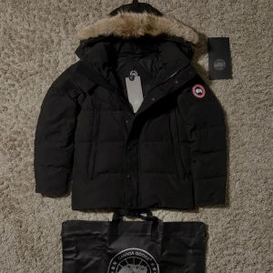 Svart dunjacka från Canada Goose - Säljer min jätte fina svarta dunjacka från Canada Goose med avtagbar coyote päls på huvan. Jackan har en klassisk design med dragkedja och knappar framtill samt en ikonisk logga på ärmen. Perfekt för kalla vinterdagar. Storleken på jackan är S och den är knappast använd. Skriv vid intressen!